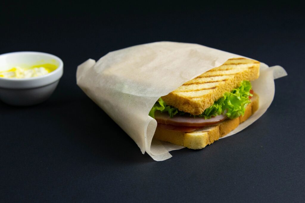 Sandwich of several slices of white bread on a wooden board. The filling of the sandwich consists of cheese and ham