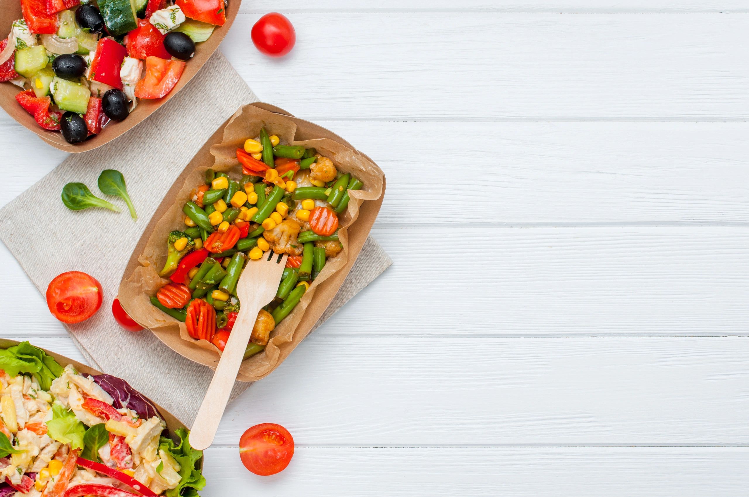 Vegetable salads in brown kraft paper food containers on white wooden background