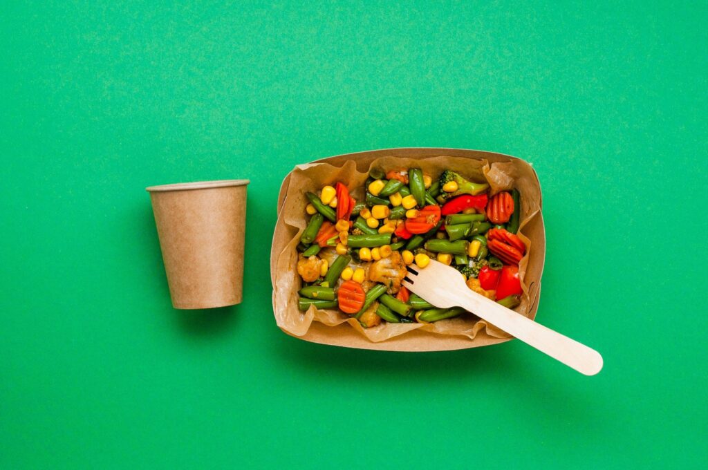 Steamed vegetables in the brown kraft paper food containers on green background