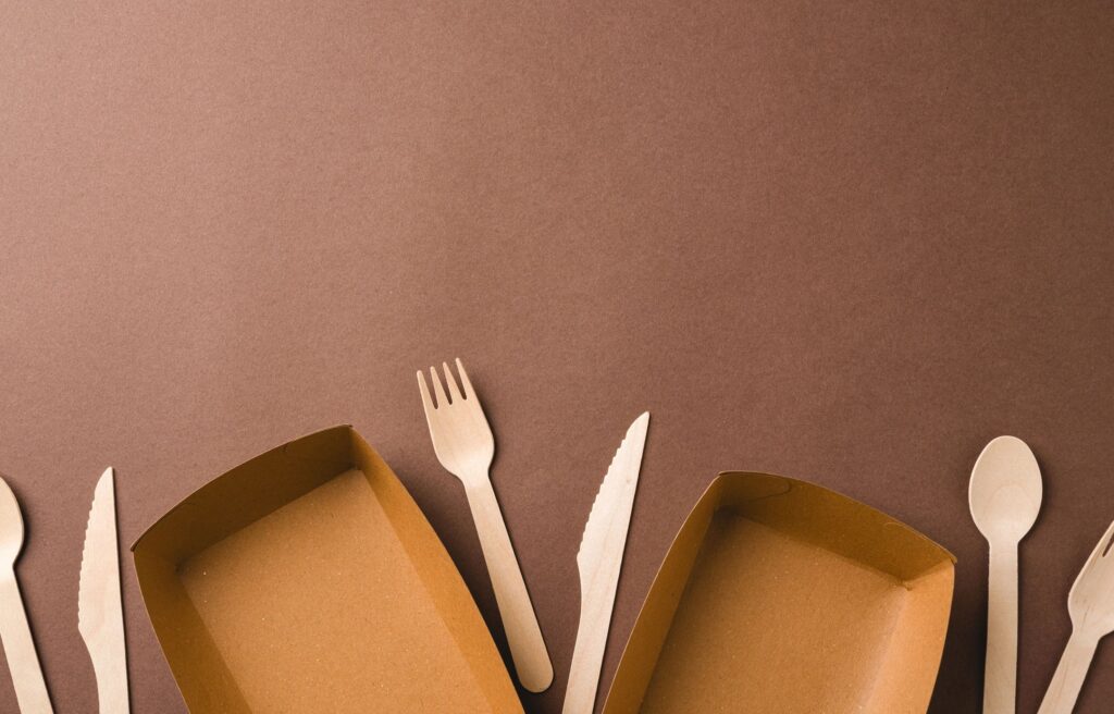 Wooden utensils and kraft trays on brown background